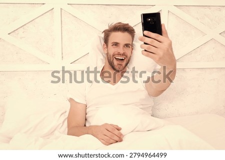 Man lying in bed making selfie. Happy man taking selfie using smartphone on bed. Video call. Blogger making content. Millennial man making selfie on phone. Video blog of blogger