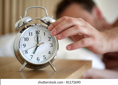Man lying in bed turning off an alarm clock in the morning at 7am