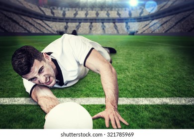 Man lying down while holding ball against large football stadium with lights