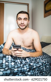 Man Lying In Morning Bed With Phone Using App Or Reading News Feed