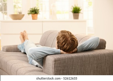 Man Lying On Back On Sofa In  Bright Living Room.