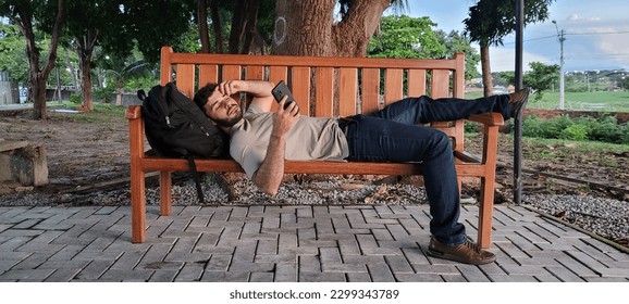 Man lying on bench looking at cell phone. Relaxing near the Parangaba Lagoon in Fortaleza.
