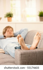 Man Lying On Couch Relaxing With Bare Feet Up At Home In Sunny Living Room.?