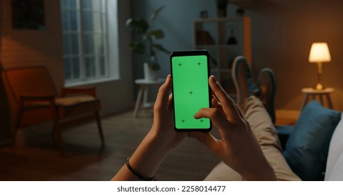 Man lying on couch using smartphone with chroma key green screen at night, scrdoing various gestures like swiping and scrolling - internet, communications concept close up  - Powered by Shutterstock