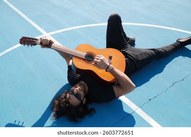 Man Lying On The Ground Plays Classical Guitar On Blue Floor Outdoor