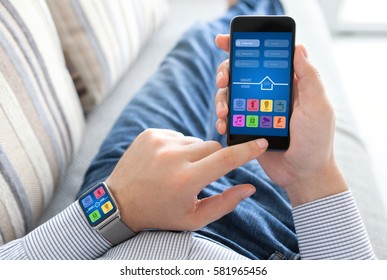 man lying on sofa holding watch and phone with app smart home on screen