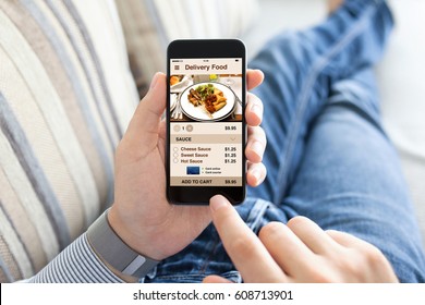 Man Lying On Sofa And Holding Phone With App Delivery Food Screen