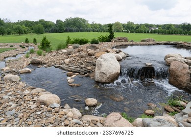 a man made pond with waterfall surrounded by stones and greenery background