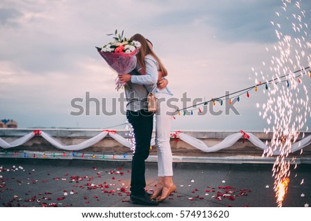 The man made a proposal to marry the girl.
A man holding his beloved girl. On the duck buildings. Romance on the roof. Sparks cold fountains and flowers