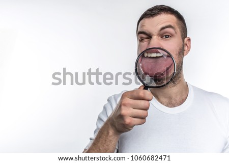 Man with magnifying glass is looking straight ahead and showing his tongue through the glass. Isolated on white background.