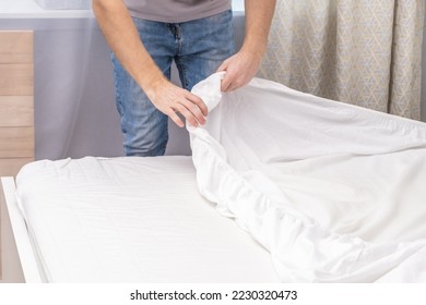A man makes his cozy bed with fresh bright white bed linen. Making the bed with fresh bed linen by a white man. The day of the change of bedclothes. The day of washing bedclothes in the laundry room. - Shutterstock ID 2230320473