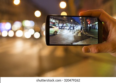 Man Makes A Picture In The Street With His Mobile Phone. Night Light Bokeh Background