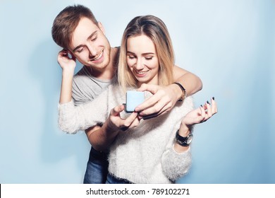 Man Makes Present To His Girl. Blue Background. Young Man Giving A Gift. Couple Offering To Each Other Gifts For Lover's Valentine Day. Valentine Couple. Family. Boy Gives To His Girlfriend Jewelry.