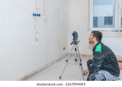 Man makes repairs in new apartment. Builder levels walls using laser level. High quality photo - Shutterstock ID 2267094093