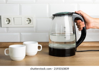 A man makes tea using boiling water from an electric kettle in the kitchen at home. It's time to have breakfast and drink tea. Modern electric kettle on a wooden table. Kettle for boiling water.