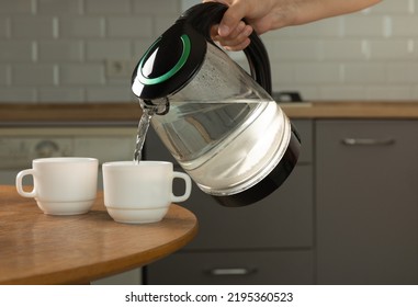 A man makes tea using boiling water from an electric kettle in the kitchen at home. It's time to have breakfast and drink tea. Modern electric kettle on a wooden table. Kettle for boiling water. - Powered by Shutterstock