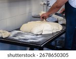A man is making bread on a table. The bread is in the process of being shaped and is covered in flour