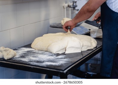 A man is making bread on a table. The bread is in the process of being shaped and is covered in flour
