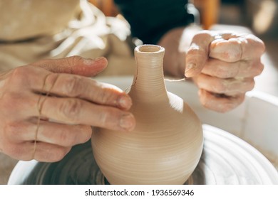 Man making by hands and thread on the pottery wheel small brown clay pot