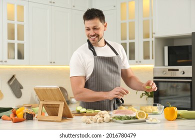 Man Making Dinner While Watching Online Cooking Course Via Tablet In Kitchen