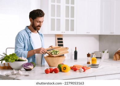 Man making dinner while watching online cooking course via laptop in kitchen - Powered by Shutterstock