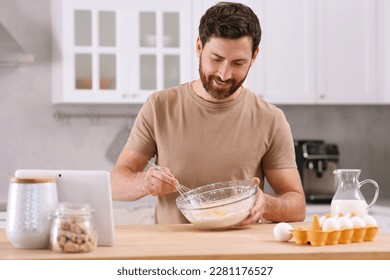 Man making dough while watching online cooking course via tablet in kitchen - Powered by Shutterstock