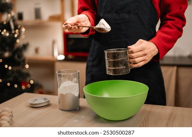 A man making gingerbread cookies on Christmas Eve pours flour into a sieve to make a soft dough. Close-up - Powered by Shutterstock