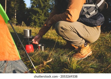 Man Making Hot Drink With Portable Gas Burner Near Camping Tent, Closeup