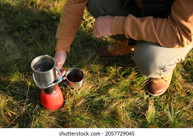 Man Making Hot Drink With Portable Gas Burner On Green Grass, Closeup. Camping Season