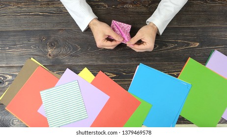 Man Making Pink Paper Crane. Multicolored Paper Sheets For Artwork, Top View. How To Make Origami Orizuru Instructions.