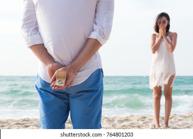 man making proposal with engagement ring and gift box to his woman at sea beach - wedding concept