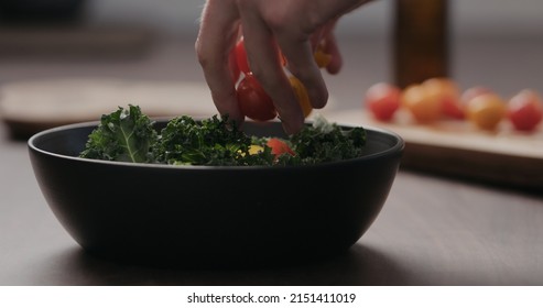 Man Making Salad With Kale, And Cherry Tomatoes In Black Bowl On Concrete Countertop, Wide Photo