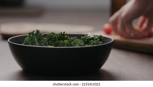 Man Making Salad With Kale, And Cherry Tomatoes In Black Bowl On Concrete Countertop, Wide Photo