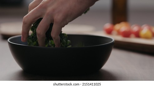 Man Making Salad With Kale, And Cherry Tomatoes In Black Bowl On Concrete Countertop, Wide Photo