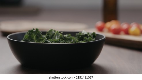 Man Making Salad With Kale, And Cherry Tomatoes In Black Bowl On Concrete Countertop, Wide Photo