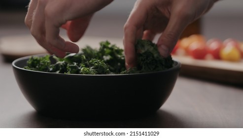 Man Making Salad With Kale, And Cherry Tomatoes In Black Bowl On Concrete Countertop, Wide Photo