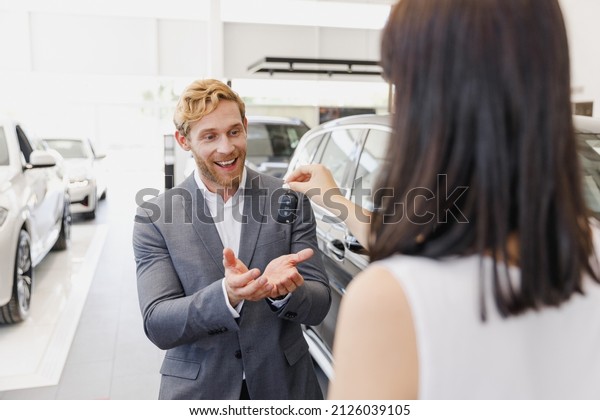 Man male smiling customer client buyer 20s\
wearing classic grey suit choose auto want buy new car automobile\
take keys from salesman in showroom salon dealership store motor\
show indoor. Sale concept.