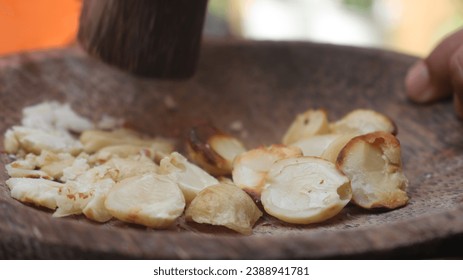 A man manually grinds garlic cloves in a wooden mortar - Powered by Shutterstock