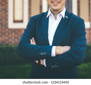 Man In Marine Blue Suit With Arms Crossed Stands Near The Brick House