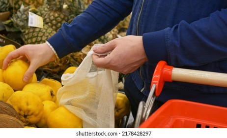 A Man In The Market Buys Fresh Fruit. Ripe Yellow Fruits Are Selected On The Shelf In The Store And Put In A Reusable Bag. Yellow Quince Selection In The Grocery Supermarket. Buying Fruit From Farmers