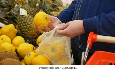 A Man In The Market Buys Fresh Fruit. Ripe Yellow Fruits Are Selected On The Shelf In The Store And Put In A Reusable Bag. Yellow Quince Selection In The Grocery Supermarket. Buying Fruit From Farmers