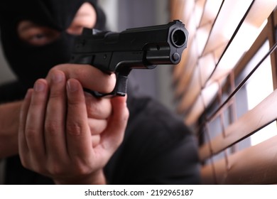 Man in mask aiming through window blinds indoors, focus on hands