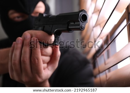 Man in mask aiming through window blinds indoors, focus on hands