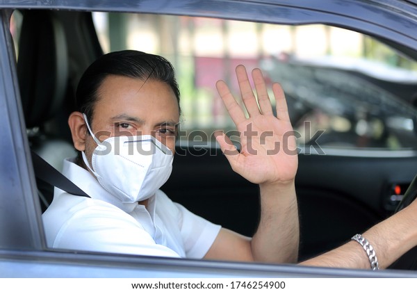 Man in mask driving\
car and waving good bye. Protection against covid-19. Drive safely.\
Take Care.