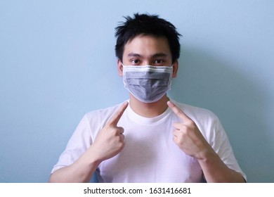 Man with mask gesture his hand point his index finger to disease protection mask on his face isolated in blue background. disease protection concept - Shutterstock ID 1631416681