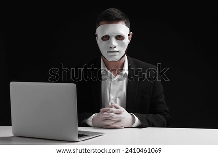 Man in mask and gloves sitting with laptop at white table against black background
