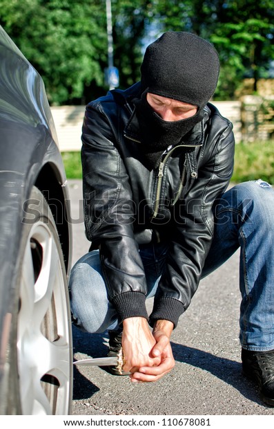 Man in mask\
punctures a car tyre. Revenge\
concept