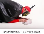 Man in the mask, red hat with devil horns and halloween costume posing with lots of money over white studio background.