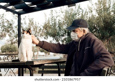 Man In Mask Strokes Stray Homeless Sitting Cat On Street, In The Park. Selective Focus.