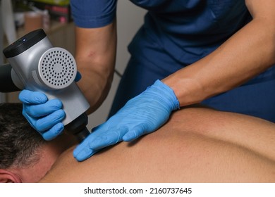 Man Massaging The Other Man's Neck With Massaging Percussion Device. Percussion Therapy.